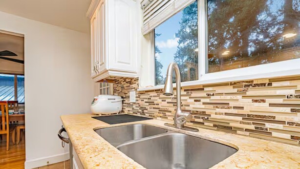 A modern kitchen with a double sink, white cabinets, and a view of trees through a large window.