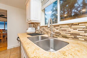 A modern kitchen with a double sink, white cabinets, and a view of trees through a large window. - Mercer Island Escape Luxury Stay (Mercer Island)