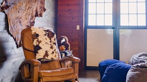 Een rustiek houten interieur met een leren fauteuil, een blauwe kruikzak en een opgehangen dierenhoofd aan de muur.