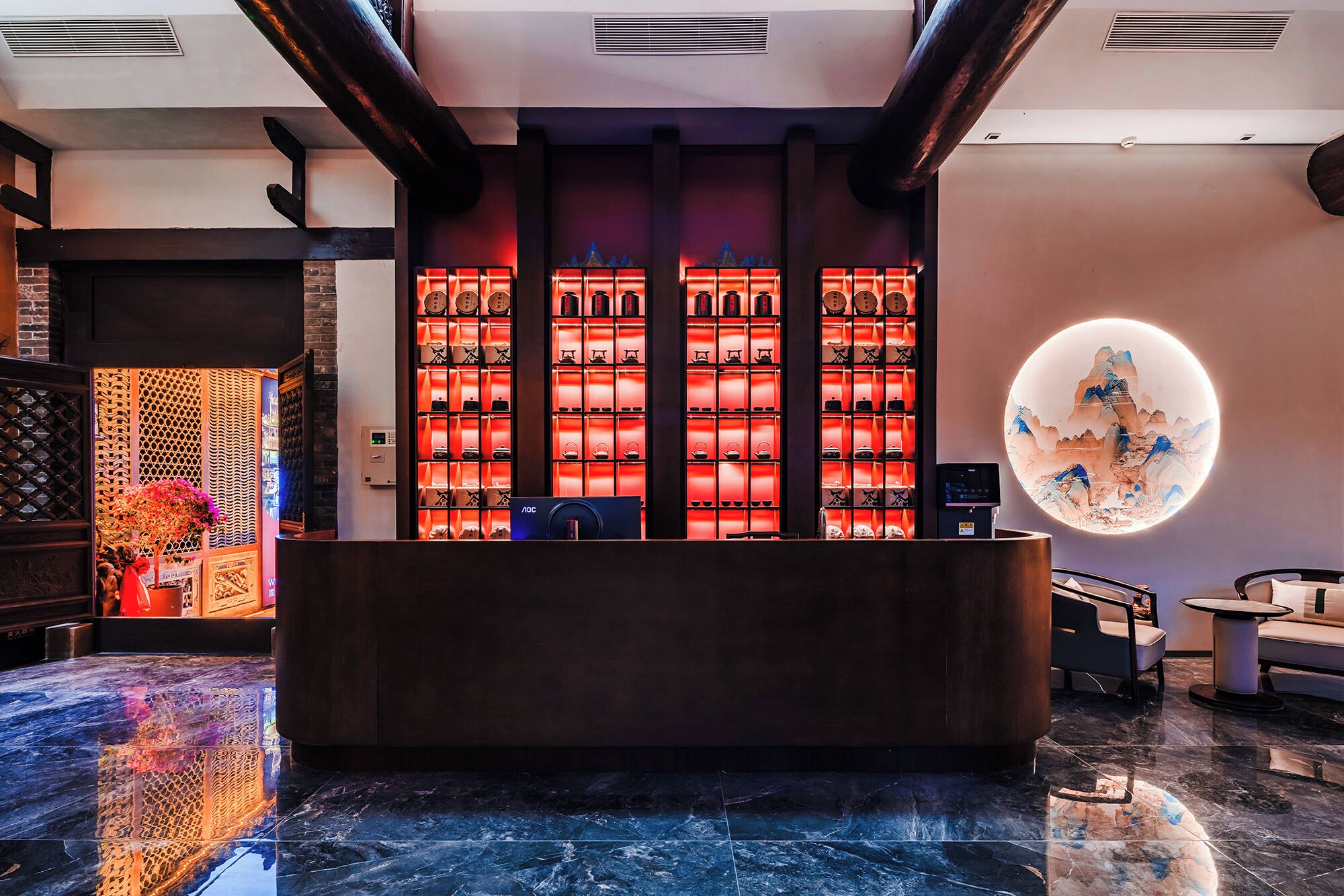 A reception area with a dark reception desk, a wall of illuminated teapots, and a circular decorative piece on the wall.