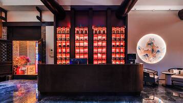 A reception area with a dark reception desk, a wall of illuminated teapots, and a circular decorative piece on the wall.