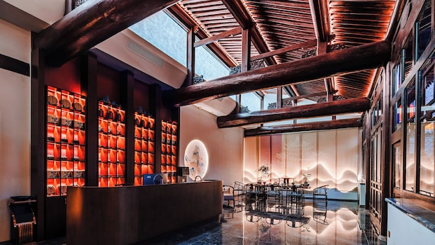 A lobby with a reception desk, seating area, and a large window with a view of a traditional building. - lishe (Jinzhong)