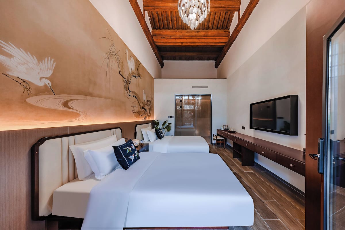 A modern hotel room with a large bed, a flat-screen TV, a wooden ceiling, and a mural on the wall.