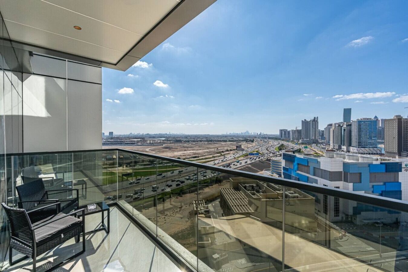 A modern hotel room with a balcony overlooking a cityscape and highway.