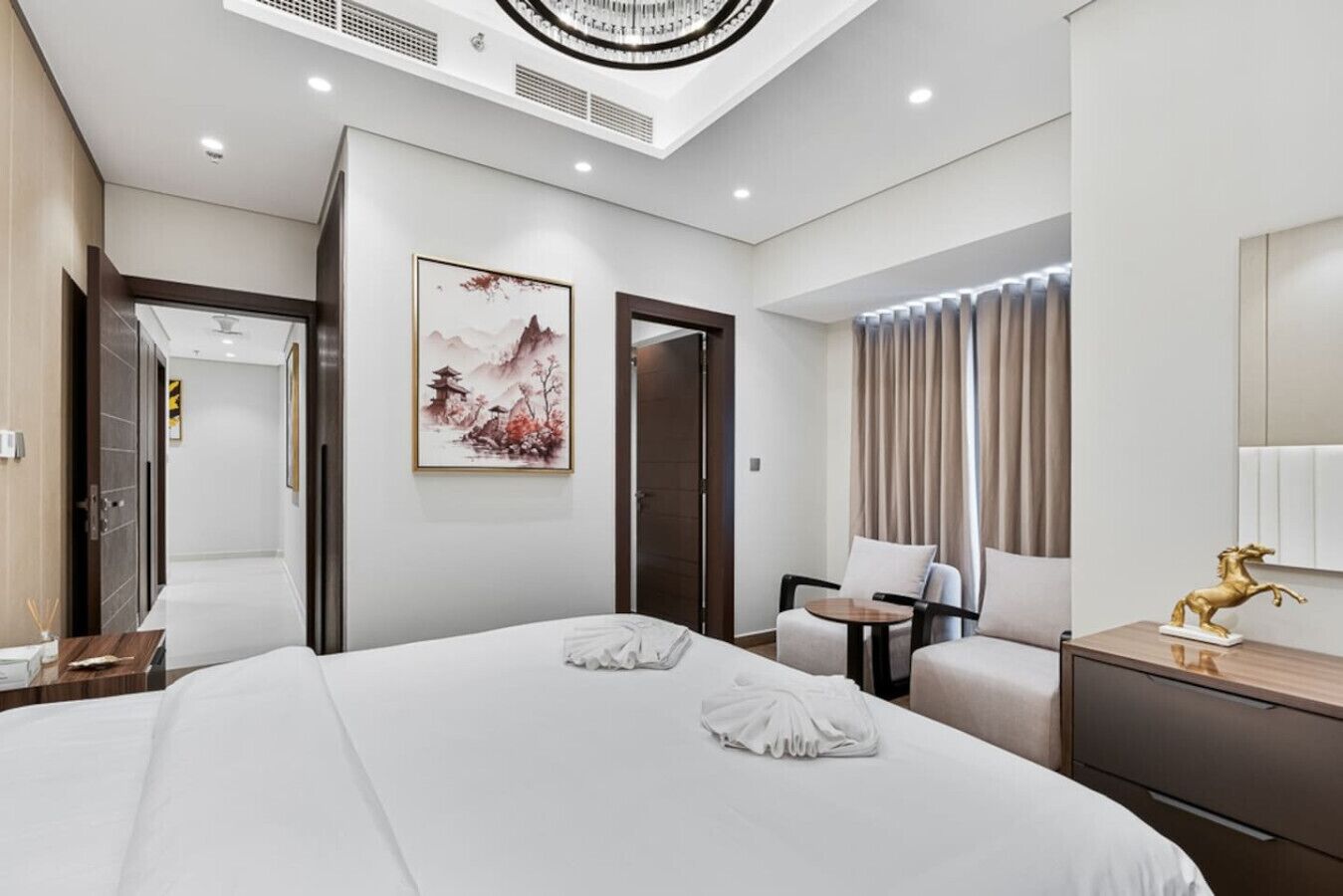 A modern hotel room with a large bed, a desk, a chair, and a painting on the wall.