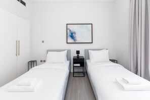 Une chambre d’hôtel avec deux lits simples, une table de chevet avec une lampe, un tableau abstrait encadré accroché au mur et une armoire.