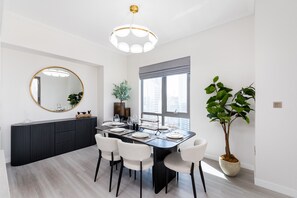 Un espace repas moderne avec une table à manger noire, des chaises blanches, un miroir rond et une plante en pot.