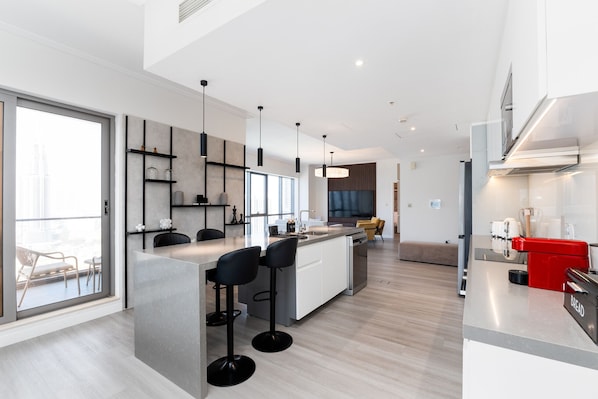 A modern kitchen with a central island, bar stools, and a red appliance.