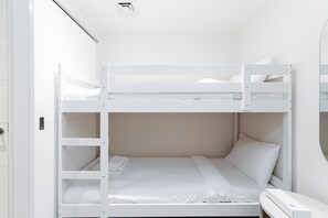 Habitación con literas, ropa de cama blanca y una mesita de noche pequeña.