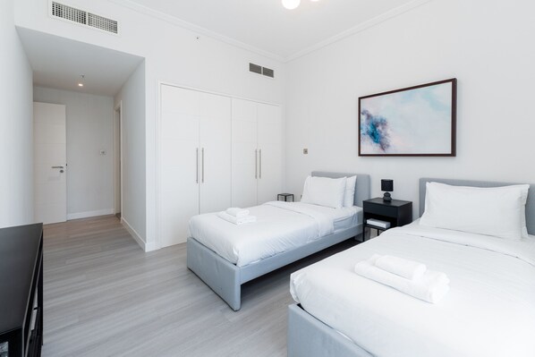 A modern hotel room with two beds, a wardrobe, a desk, and a painting on the wall.