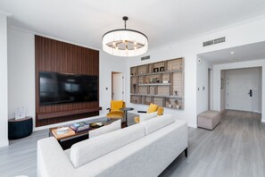 Een moderne woonkamer met een grote flatscreen televisie, een witte bank, gele fauteuils en een houten boekenkast.