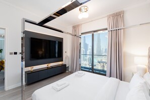 Een moderne hotelkamer met een groot bed, een flatscreen televisie aan de muur, uitzicht op de stad door grote ramen en een minimalistisch design.