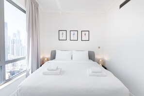 Habitación de hotel con una cama grande, ropa de cama blanca, vistas a la ciudad y tres obras de arte enmarcadas en la pared.