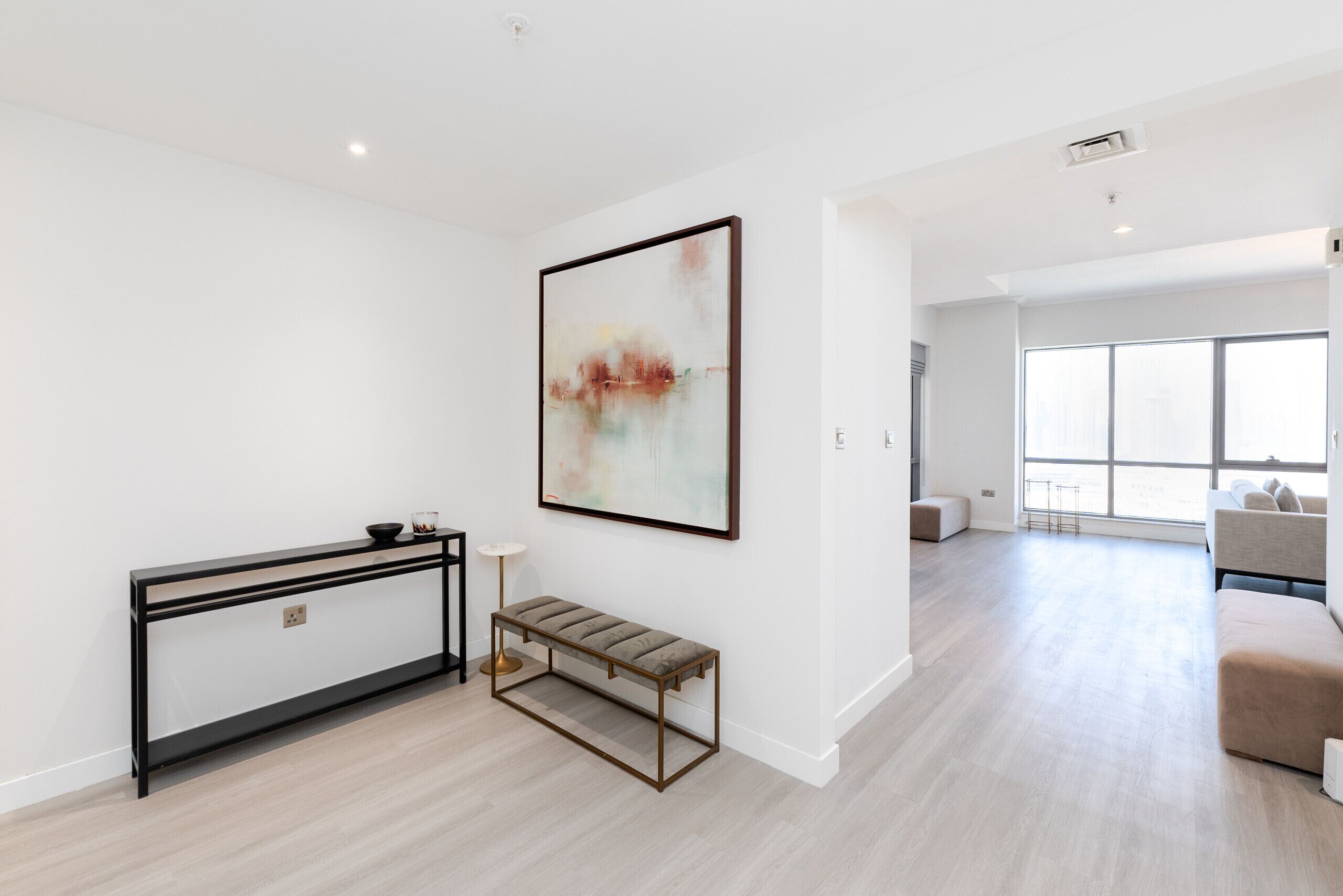 A modern living room with a console table, bench, and a large abstract painting.