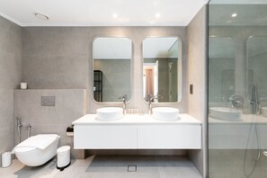 Een moderne badkamer met twee wastafels, een badkuip en een douchecabine met glazen wanden.