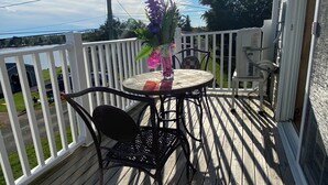Eine Holzterrasse mit rundem Tisch und Stühlen, einem weißen Geländer und Blick auf Himmel und Bäume.