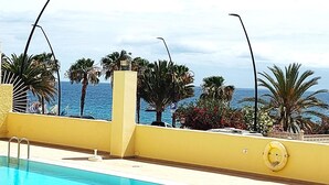 A pool area with a view of the ocean, palm trees, and a lifebuoy on the wall. - LAS VISTAS 1 BEDROOM WIFI FREE (Los Cristianos)