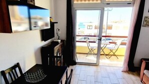 A room with a dining table, chairs, a TV mounted on the wall, a sliding glass door leading to an outdoor area with tables and chairs. - LAS VISTAS 1 BEDROOM WIFI FREE (Los Cristianos)
