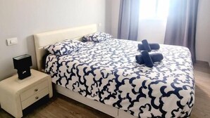 Ein ordentlich bezogenes Bett mit einem gemusterten Überwurf, ein Nachttisch mit Lampe und ein Fenster mit Vorhängen.