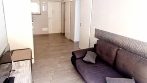 Ein modernes Wohnzimmer mit Holzboden, einem dunkelgrauen Sofa mit Kissen und einer weißen Deckenleuchte.