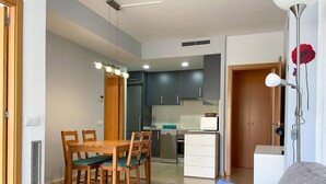 A compact living space with a dining area, kitchenette, and a sofa with cushions.