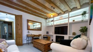 Uma sala de estar com mesa de centro de madeira, sofás brancos, televisão e lareira.