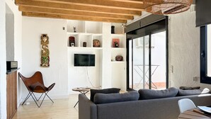 A modern living room with a grey sofa, a wooden ceiling, and a TV mounted on the wall.