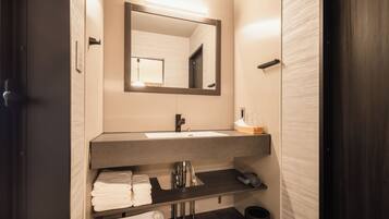 Une salle de bain moderne avec une porte en bois foncé, un grand miroir, un lavabo avec un porte-serviettes et des toilettes.
