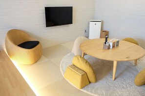 Una sala moderna con un sofá, una mesa de centro, un televisor de pantalla plana y un pequeño electrodoméstico blanco.