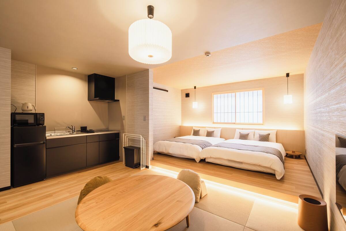 Quarto de hotel moderno com cozinha compacta, área de jantar e uma cama grande com vista para a cidade.