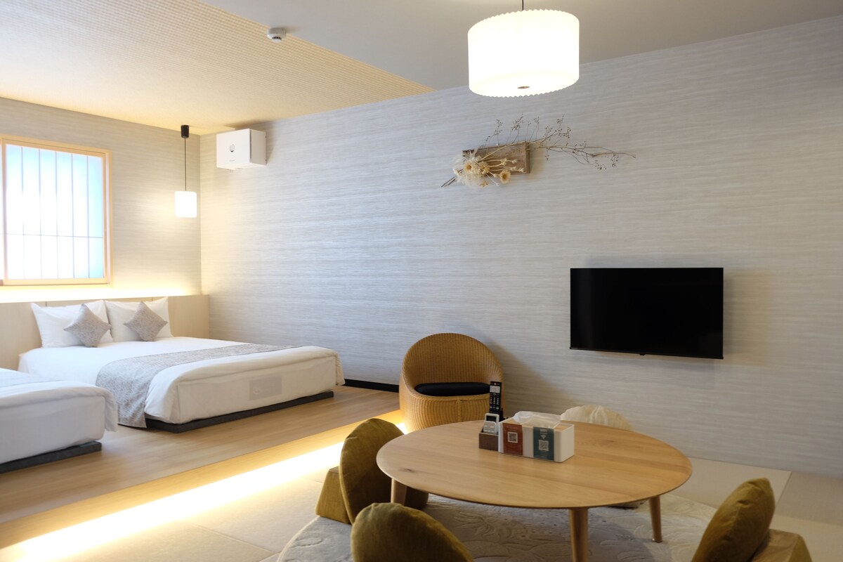 A modern hotel room with a bed, bedside table, chair, and a flat-screen TV mounted on the wall.
