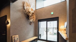 A reception area with a stone floor, a wooden bench, a wall-mounted sculpture, and a door leading outside. - BEPPU non (Beppu)