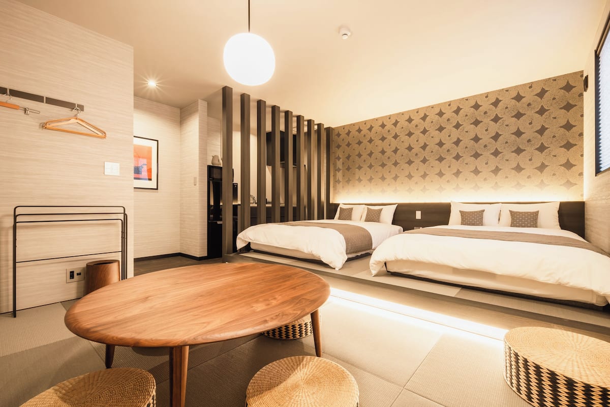 Quarto de hotel moderno com uma mesa de madeira, duas camas, um cabideiro e uma parede estampada.