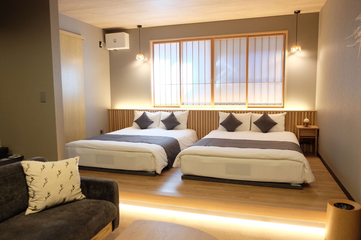 A hotel room with two beds, a sofa, a bedside table, and a window with a view.