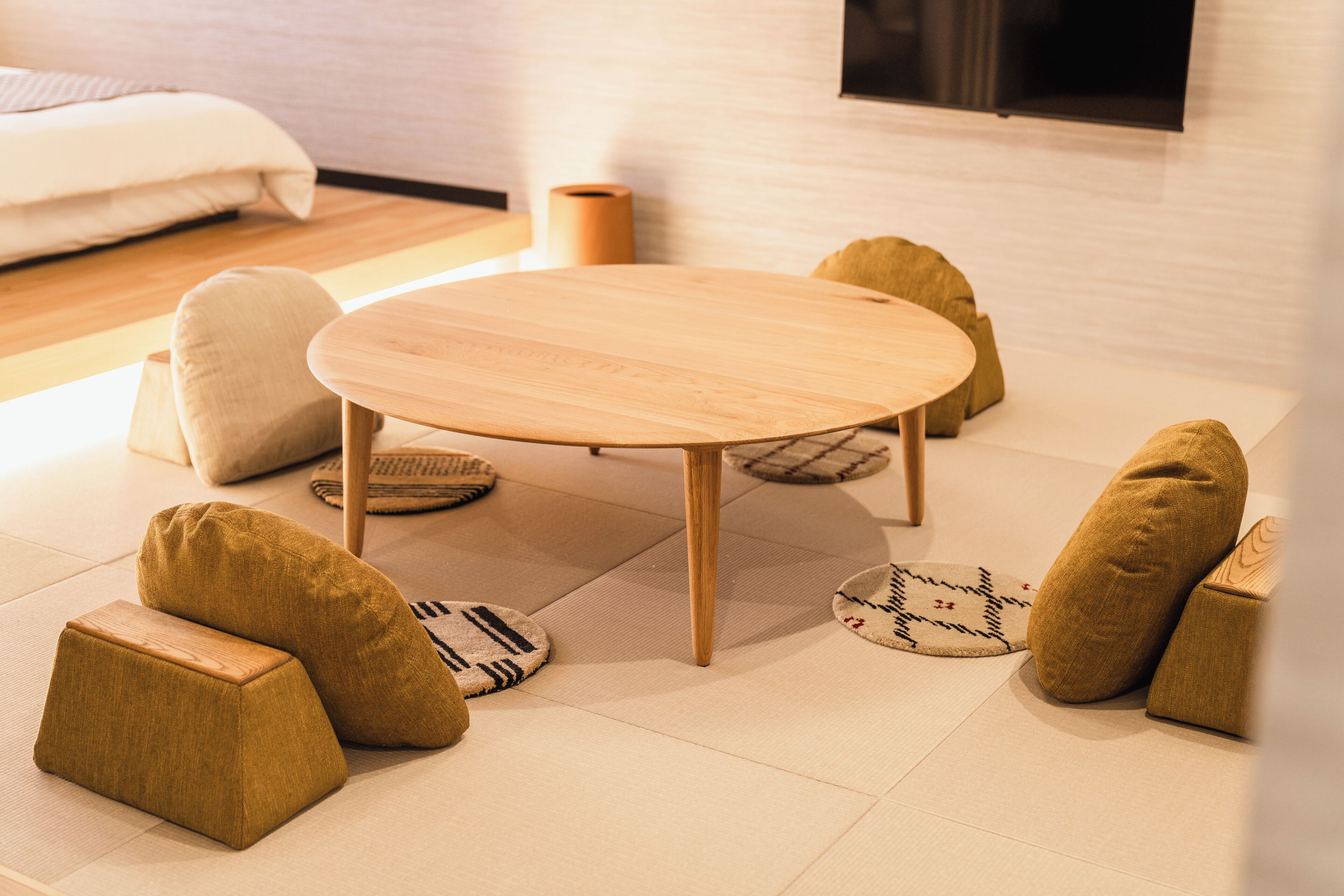 Una habitación con una mesa redonda de madera, rodeada de cuatro cojines beige y un taburete pequeño.