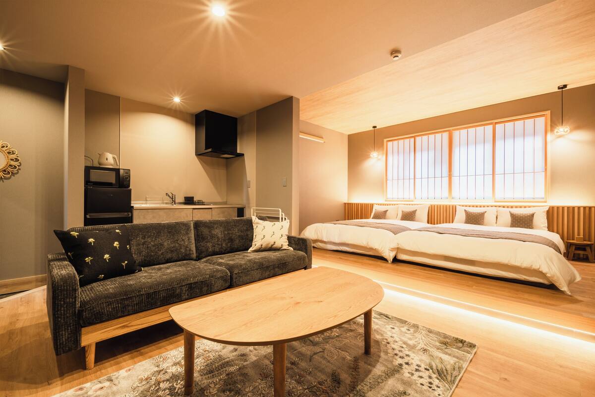 Uma sala de estar moderna com sofá, mesa de centro, área de cozinha e uma cama grande com vista para o exterior.