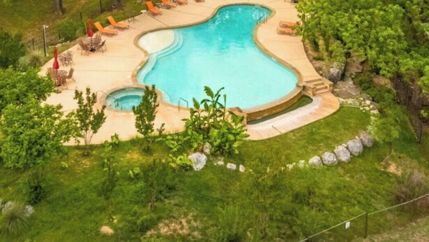 A swimming pool surrounded by lounge chairs and umbrellas, set in a lush green landscape with hills in the background.