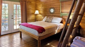 A wooden cabin bedroom with a bed, a lamp, and a window.