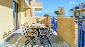 A balcony with a table and chairs, a potted plant, and a view of the sea.