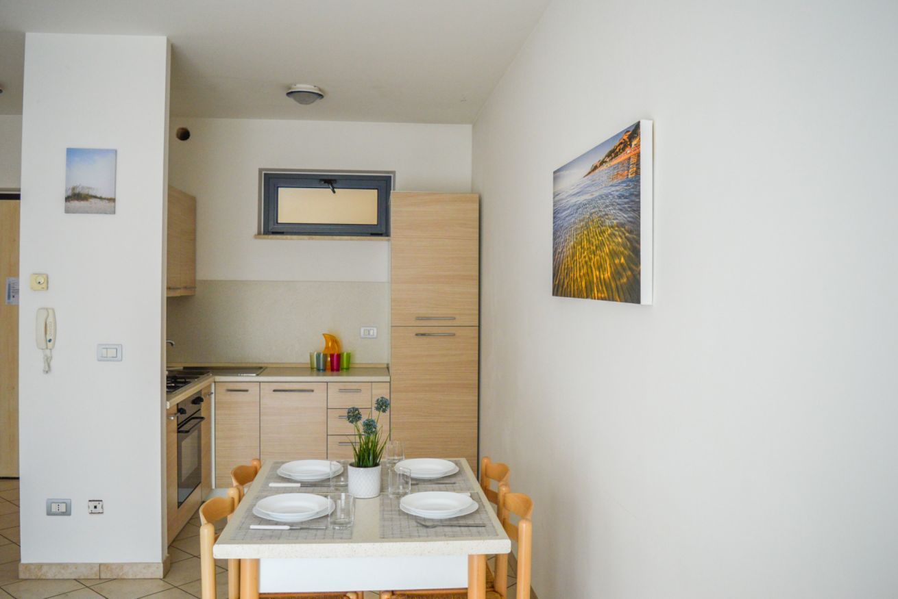 A modern kitchen with wooden cabinets, a dining table set for four, and a painting on the wall.