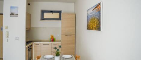A modern kitchen with wooden cabinets, a dining table set for four, and a painting on the wall.