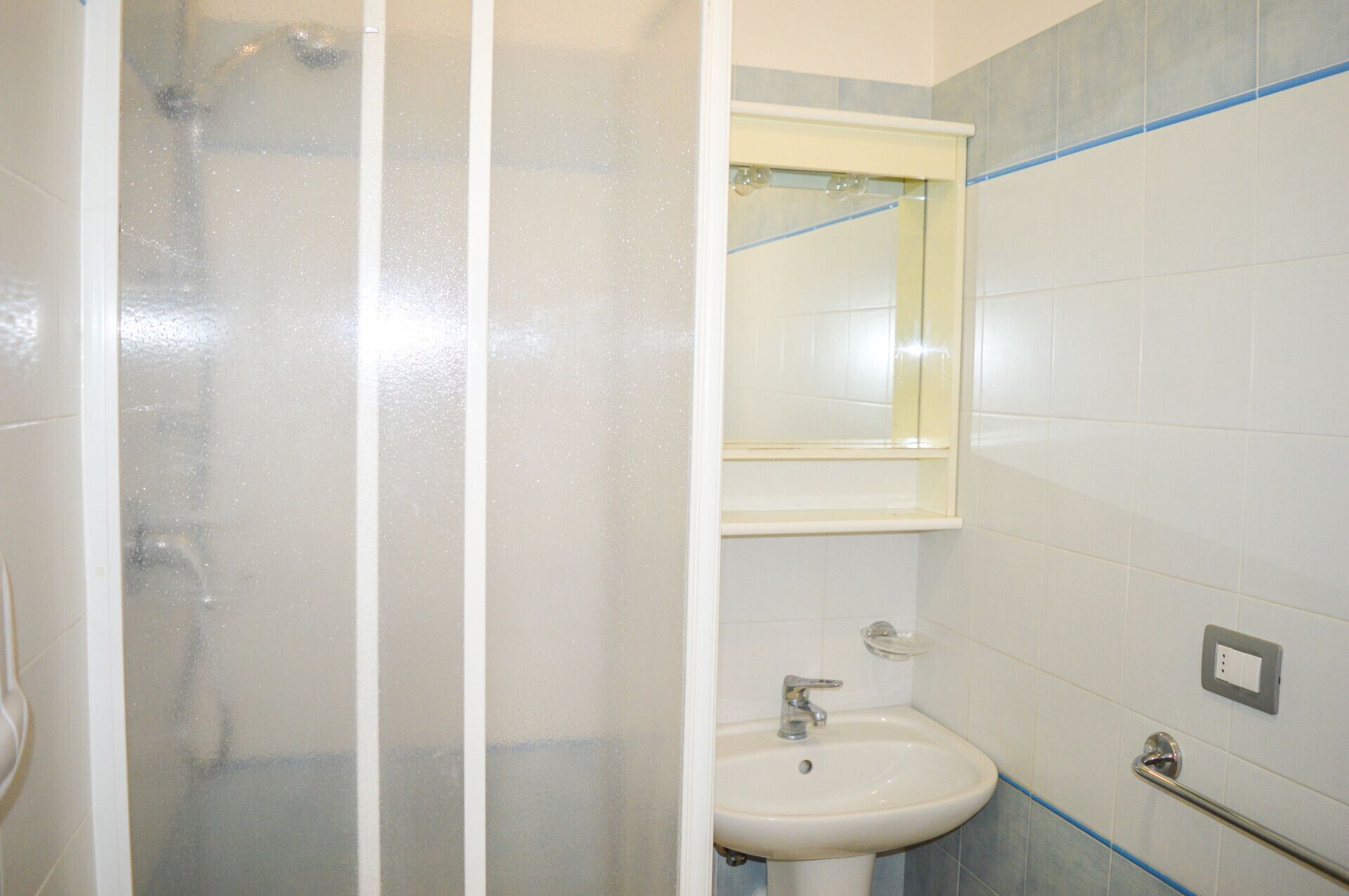 A bathroom with a shower enclosure, a sink, and a mirror.