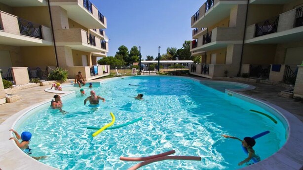 Une piscine entourée d’un immeuble à plusieurs étages doté de balcons.