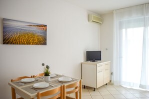 A dining area with a table set for two, a television on a cabinet, and a painting on the wall. - Homiday - Green Bay D16, 2-Bedroom Apartment (Pineto)