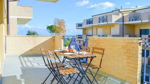 Un balcon avec une table et des chaises, un pot de fleurs et une vue sur la mer et les bâtiments.