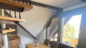A dining area with a wooden table and chairs, a staircase, and a window with a view of the outside. - Ahr valley heart (Bad Neuenahr-Ahrweiler)