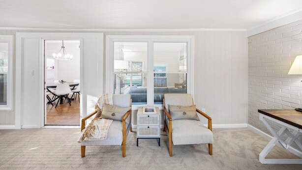 Een moderne woonkamer met twee fauteuils, een bijzettafeltje, en een eetgedeelte zichtbaar door een open deur.
