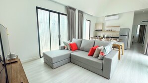 Una sala de estar moderna con un sofá seccional gris, una mesa de comedor y una cocina al fondo.