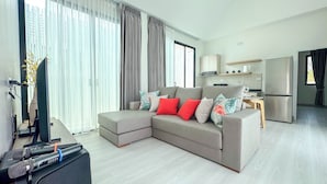 Una sala moderna con un sofá seccional, un televisor de pantalla plana y un comedor con una cocina al fondo.