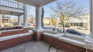 Un espacio exterior cubierto con escalones de ladrillo y columnas blancas, con vista a una calle con coches estacionados y edificios.